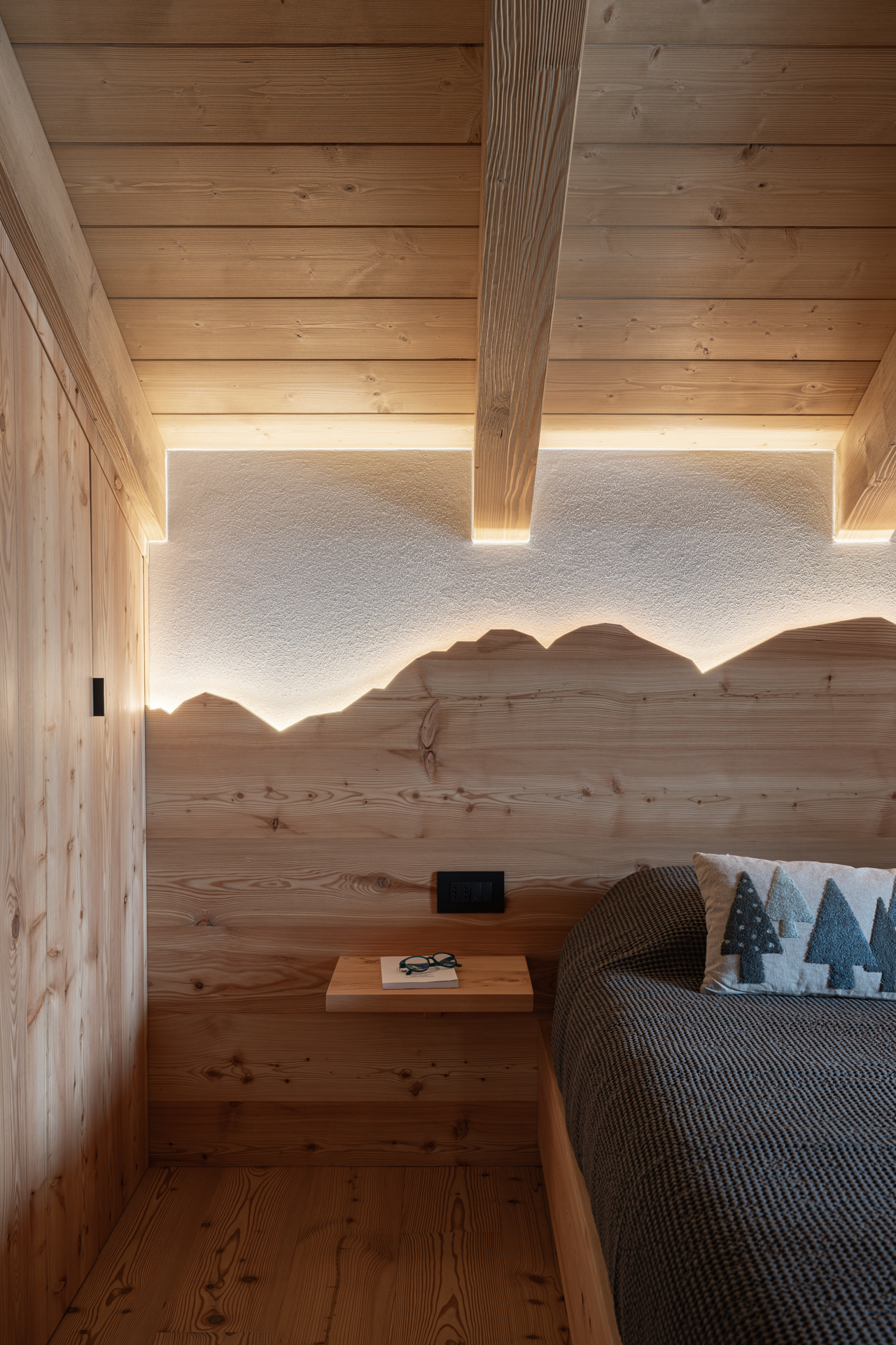 camera da letto sottotetto con armadi che seguono l'inclinazione del tetto e con testata silhouette montagne in legno realizzata su misura da Corazzolla